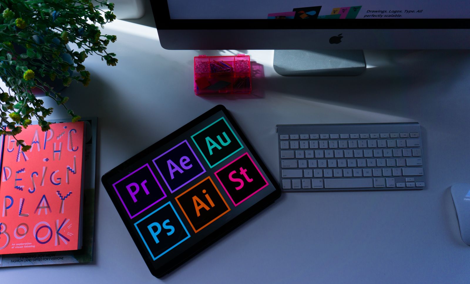 A designer's desk with a tablet of Adobe apps and a sketchbook