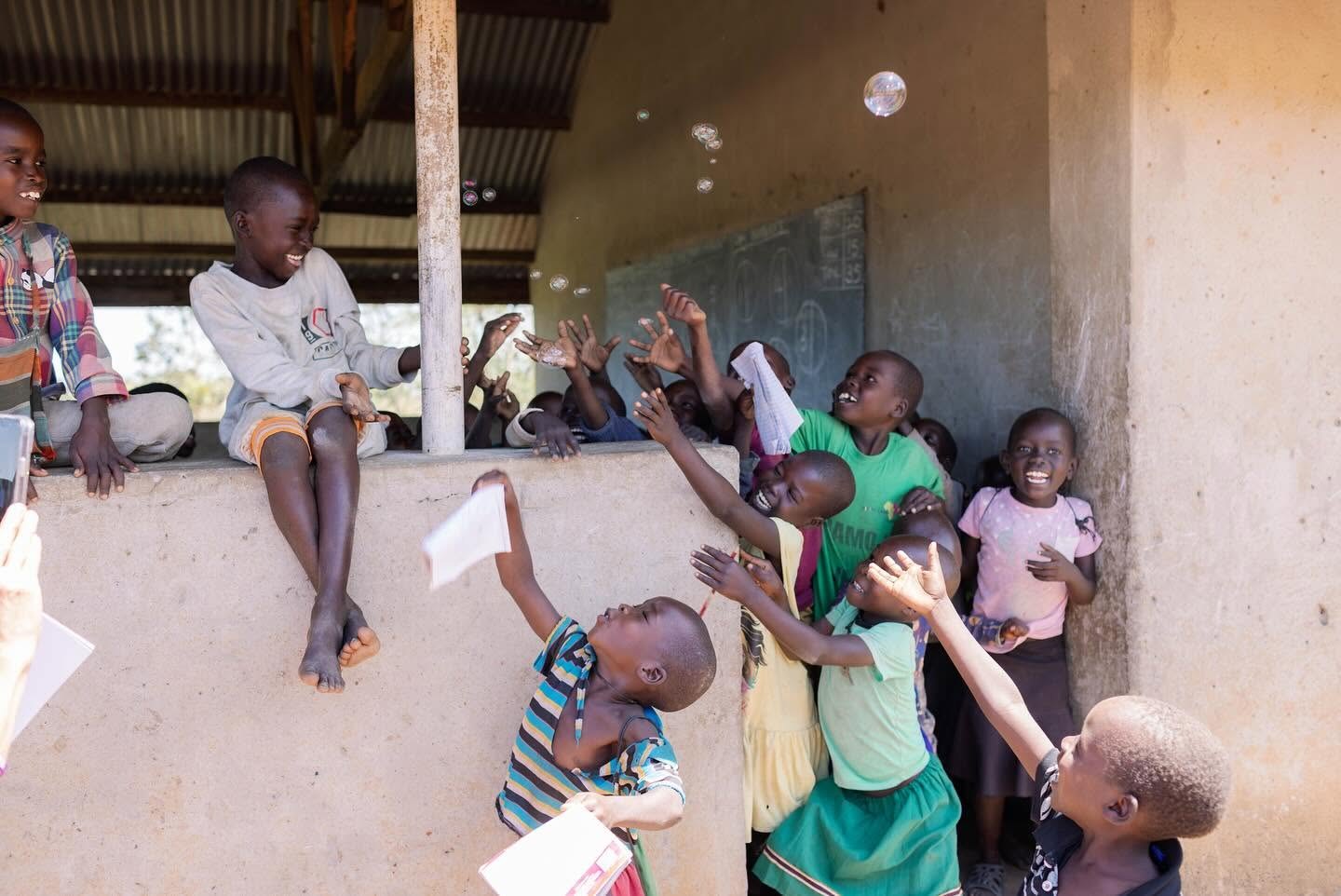 Children laughing and reaching for bubbles in an open air classroom