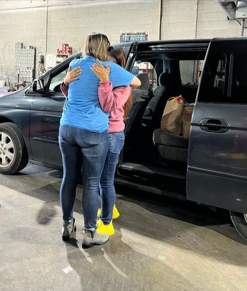 A mother hugging a volunteer beside the vehicle she has just been given